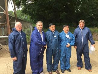 Five people stood in a row. They are wearing blue paper overalls. Two people are shaking hands